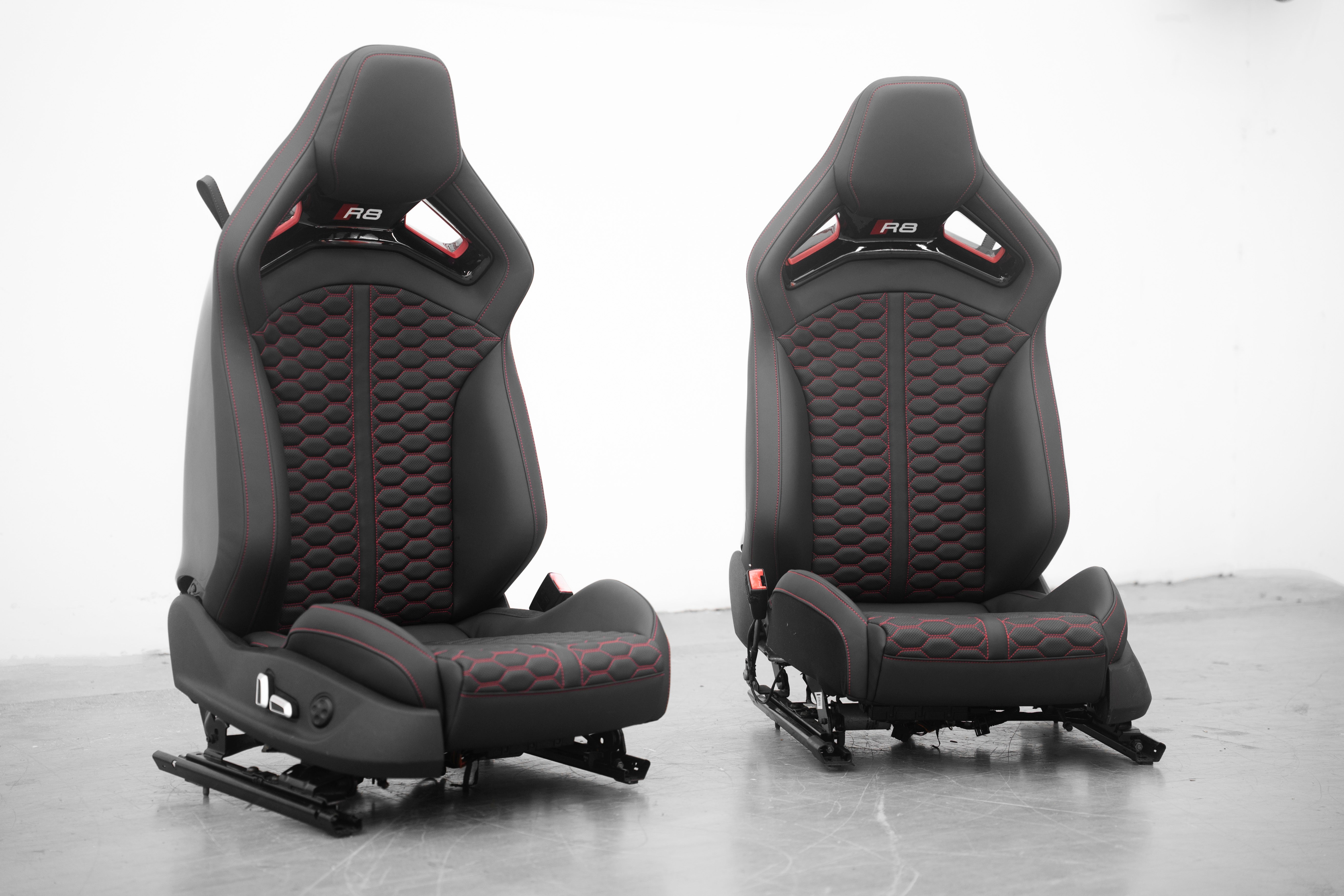 Audi R8 folding carbon fiber bucket seats shown as a pair, black leather with red honeycomb stitching and R8 logo headrests, front view