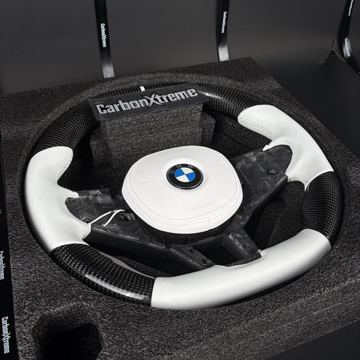 Three-quarter view of the custom carbon fiber steering wheel showing the white leather flat bottom section