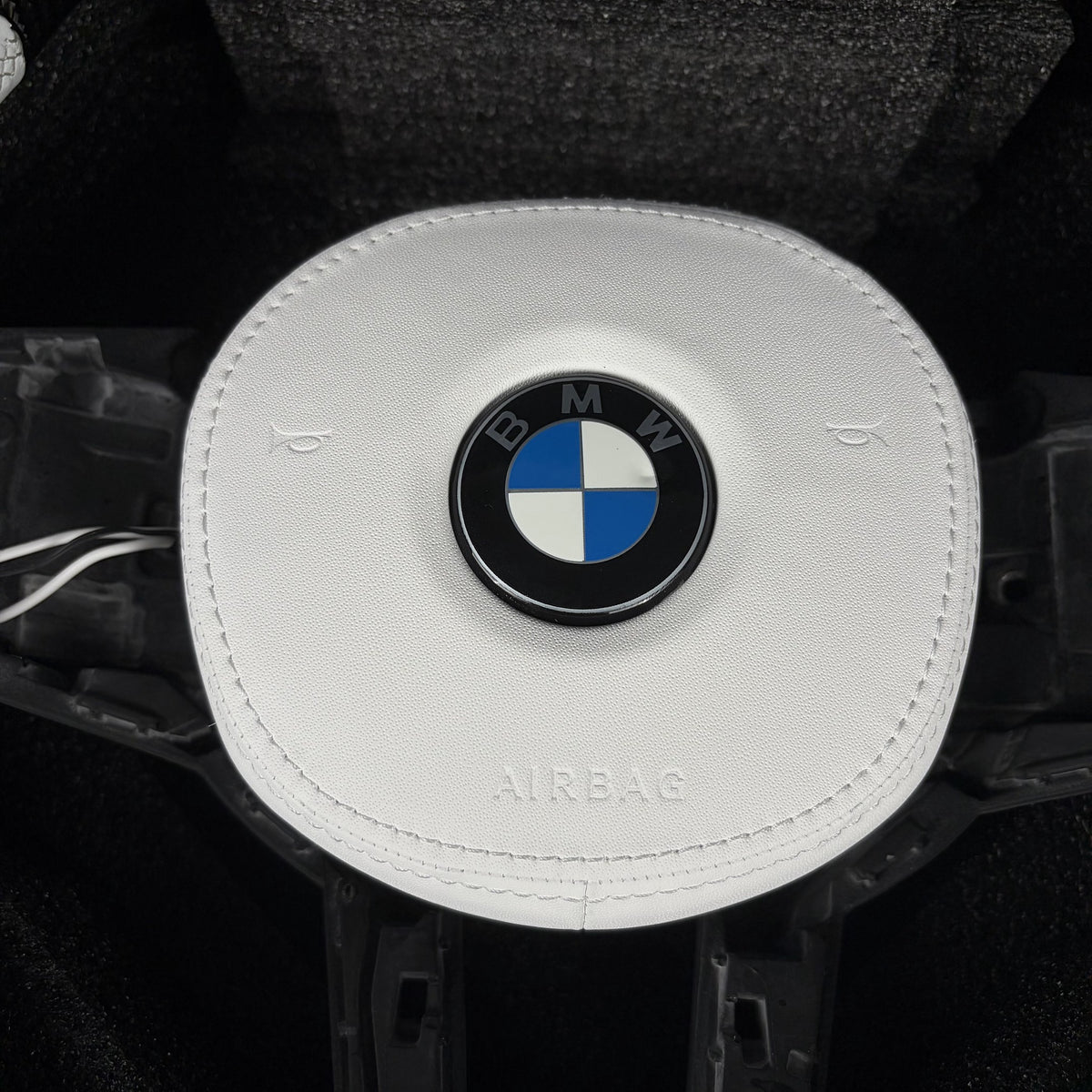 White leather airbag cover with stitched edges on the custom carbon fiber steering wheel