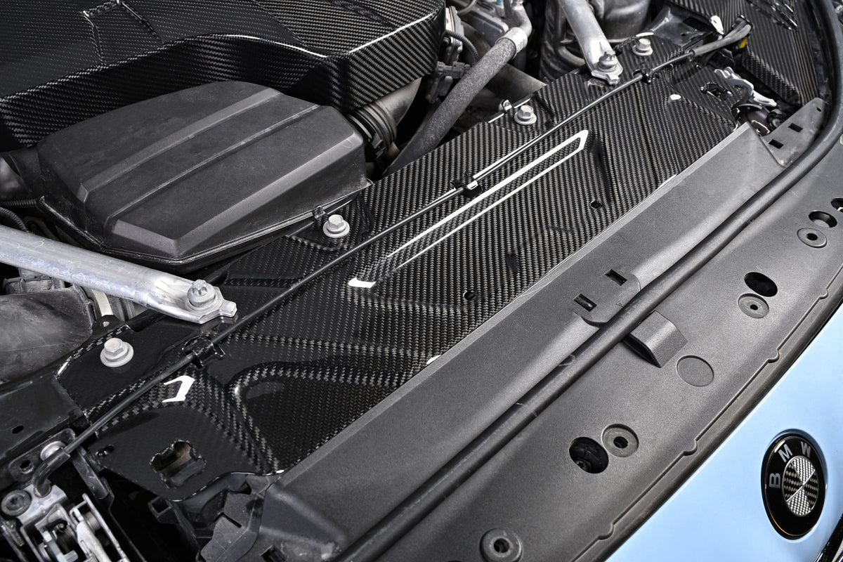 BMW G22 4 Series carbon fiber slam panel cover is shown installed across the front of a blue car at an angle.