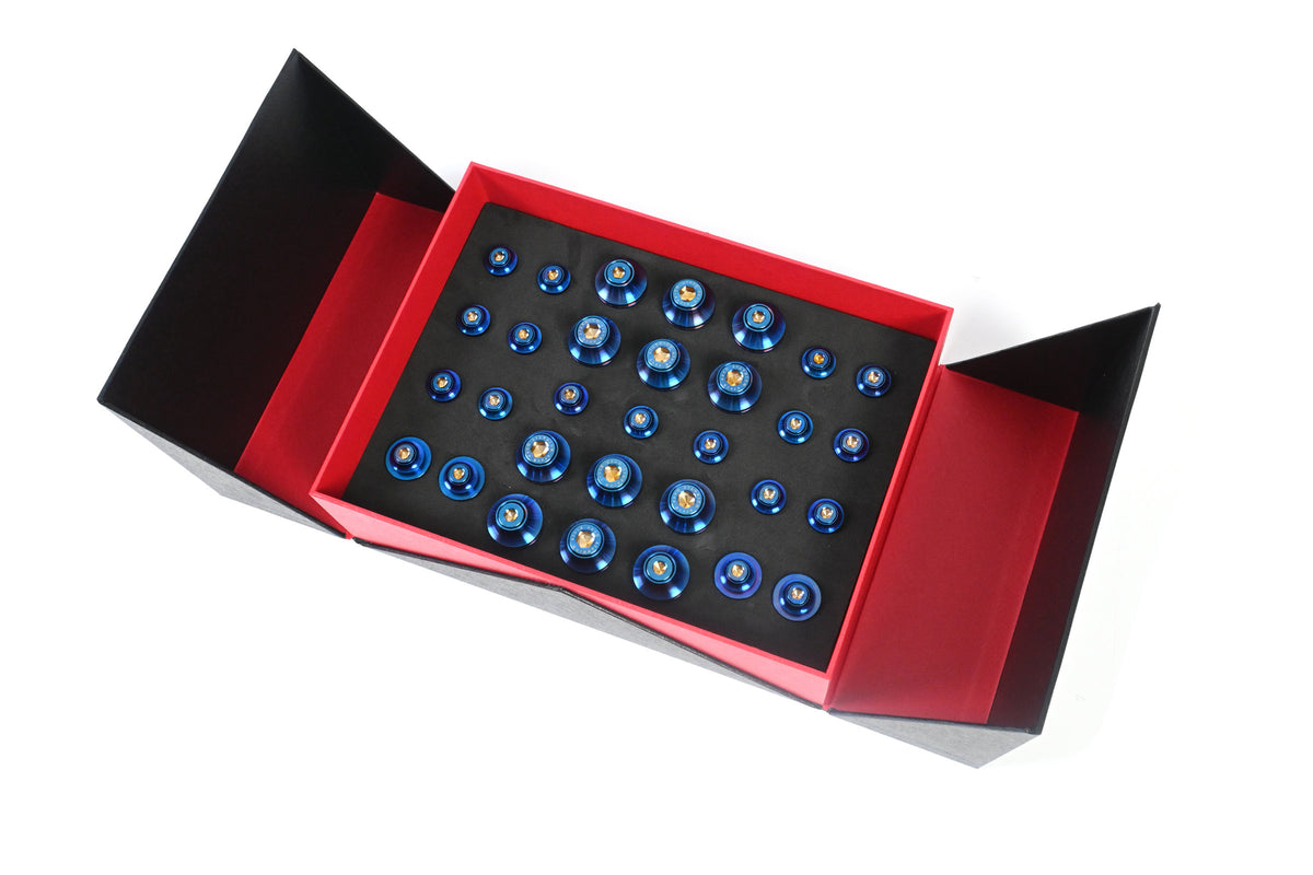 BMW G22 4 Series titanium engine bay bolt kit is shown at an angle in an open red gift box with blue bolt heads.