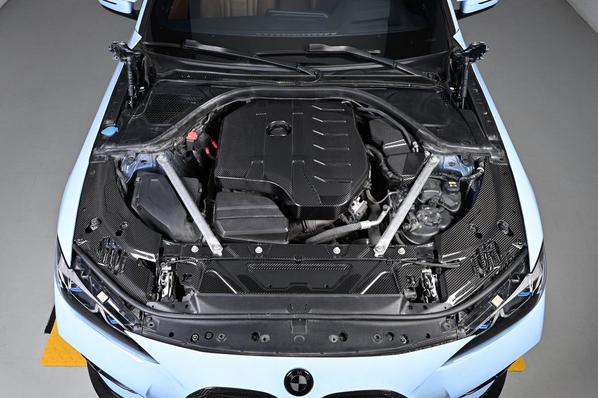 BMW 4 Series engine bay carbon fiber covers are seen from above the front of a blue car with the hood open.