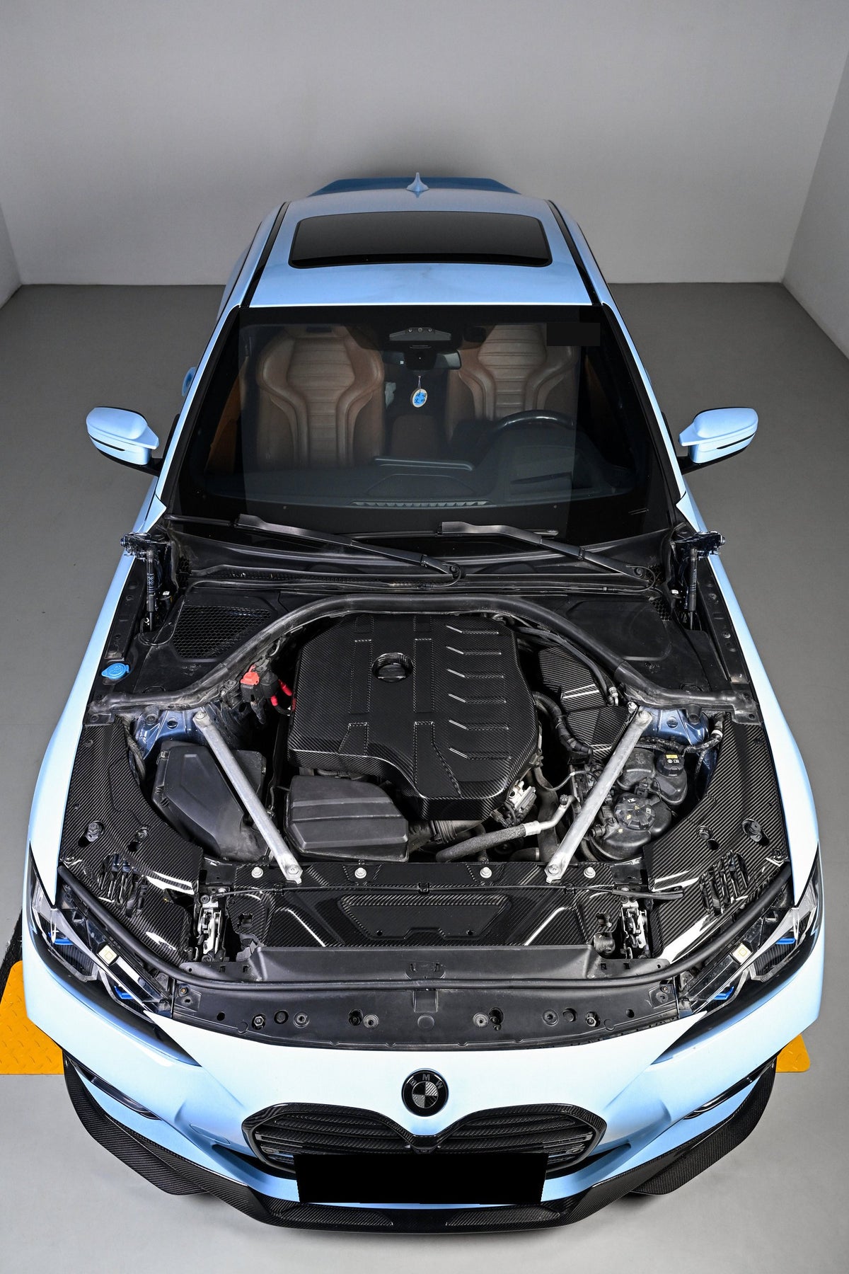 BMW 4 Series engine bay carbon fiber covers appear in a high front view of a blue car with its roof visible.