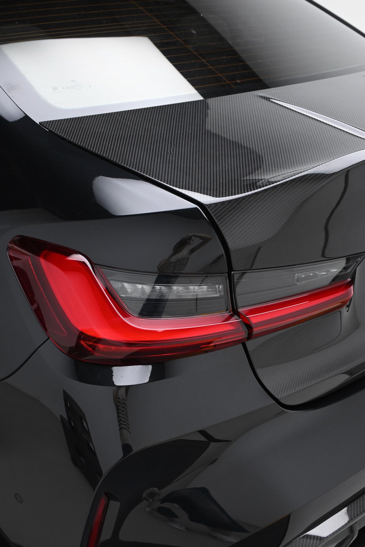 Close-up of the CSL style carbon fiber trunk lid installed on a BMW G80 M3, showing the gloss carbon weave beside the taillight