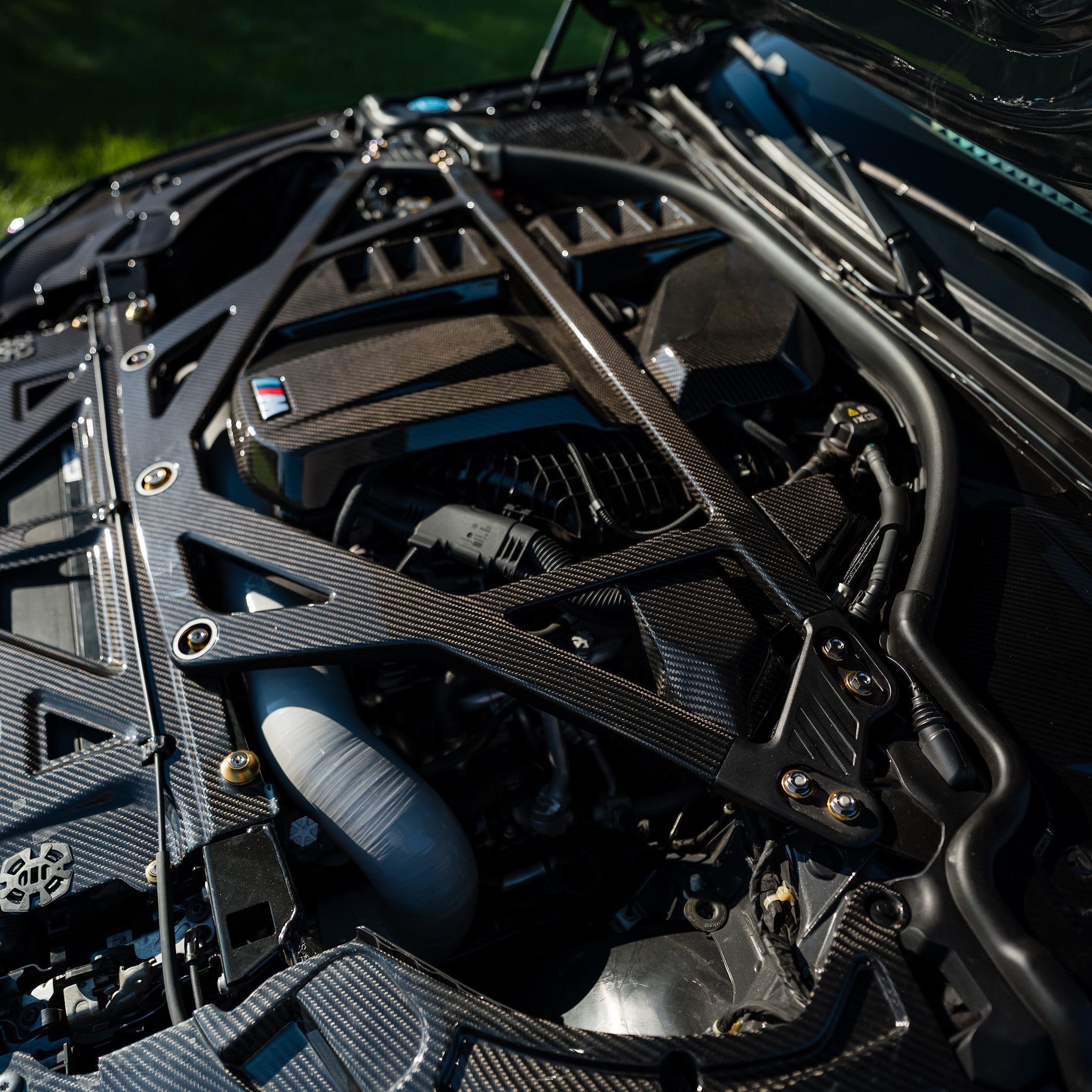 Upper-angle view of the RAG Spec carbon fiber engine bay kit installed on a BMW G80 M3