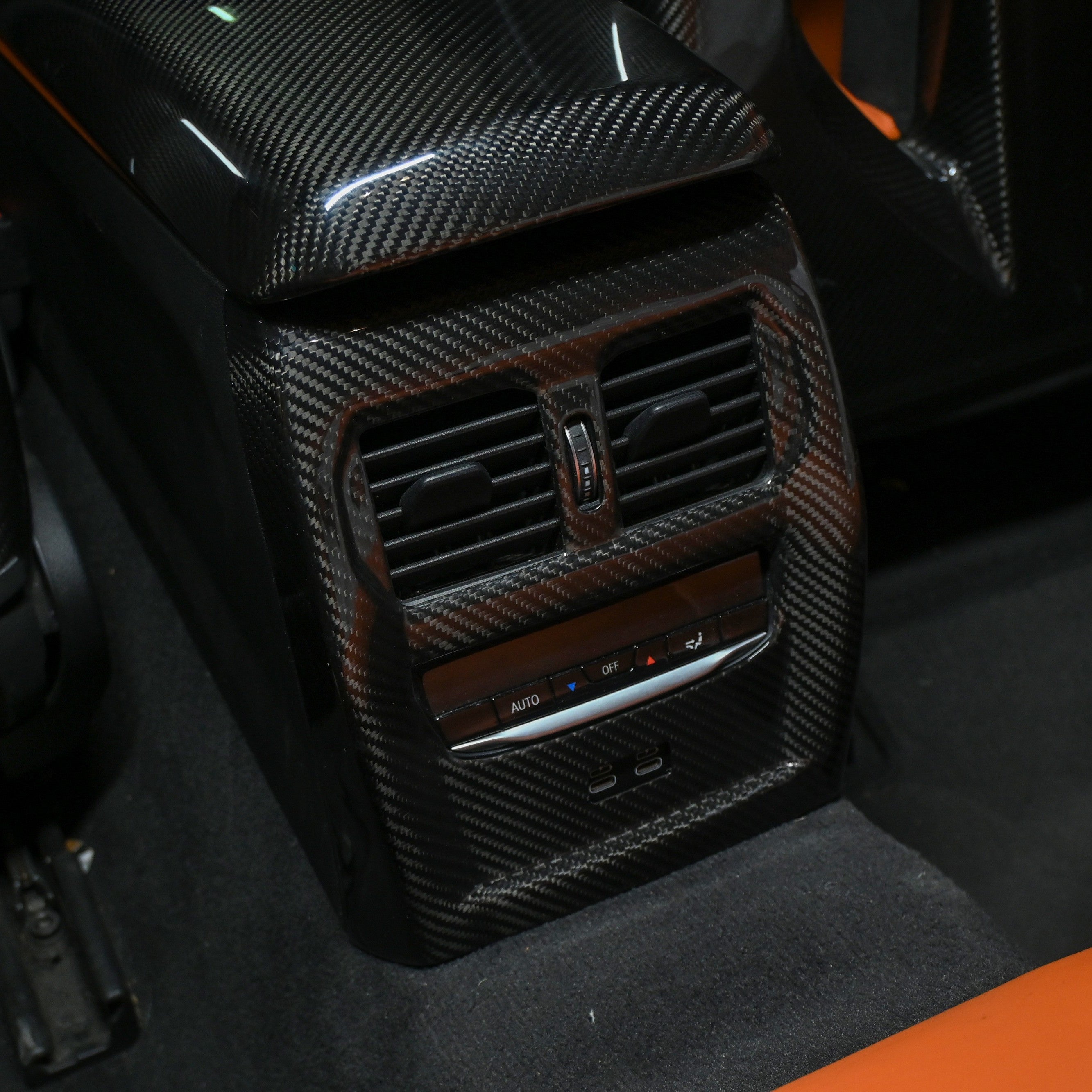 BMW M3 M4 carbon fiber armrest cover and rear vent trim installed in orange leather interior