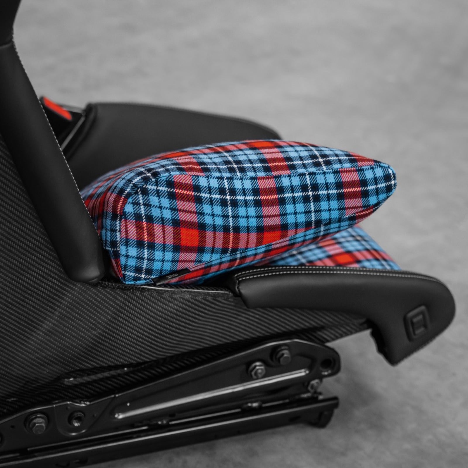 Side view of a blue and red tartan space increase pillow adding height in a Porsche 918 carbon bucket seat