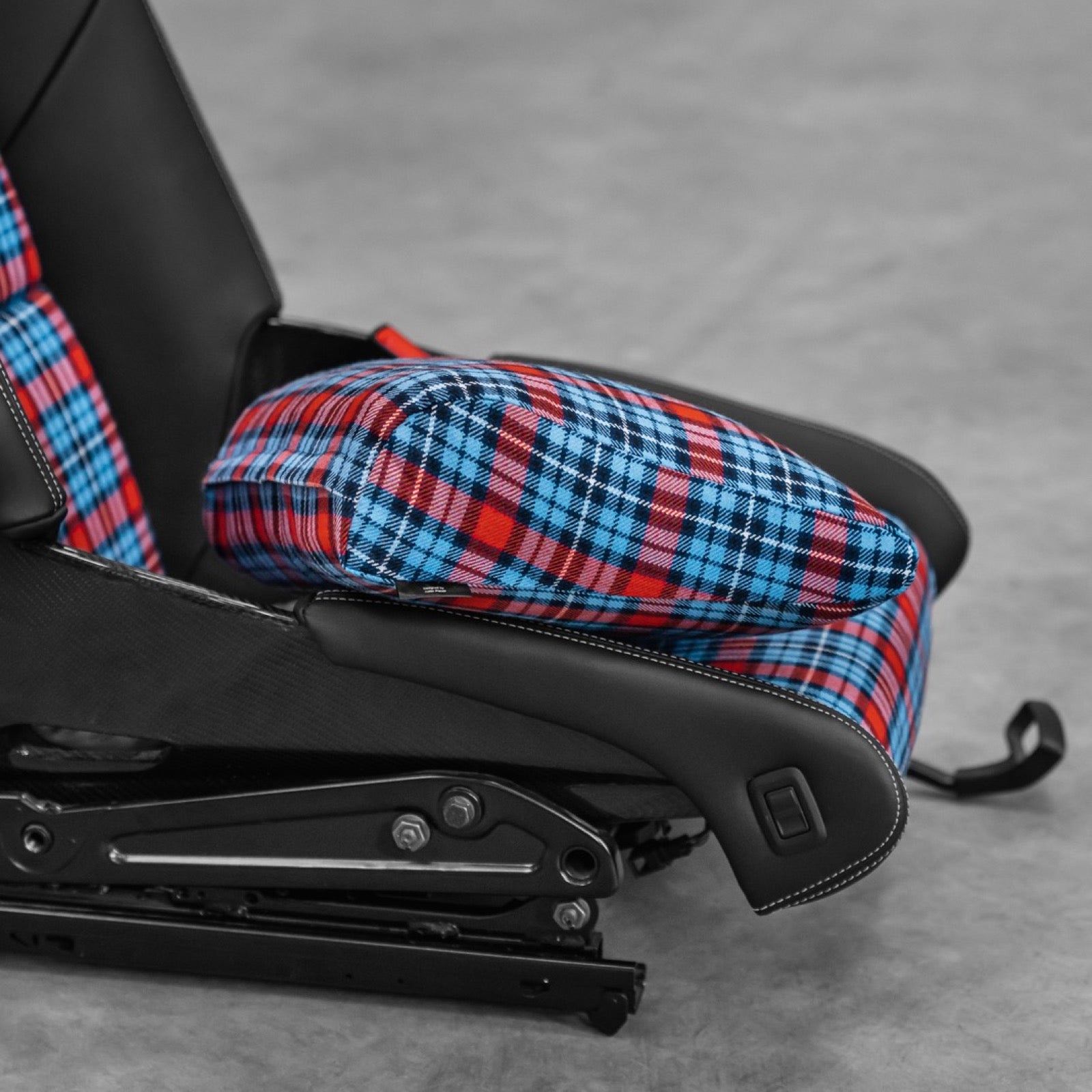 Blue and red tartan space increase cushion seated over the base of a Porsche 918 style carbon full bucket seat