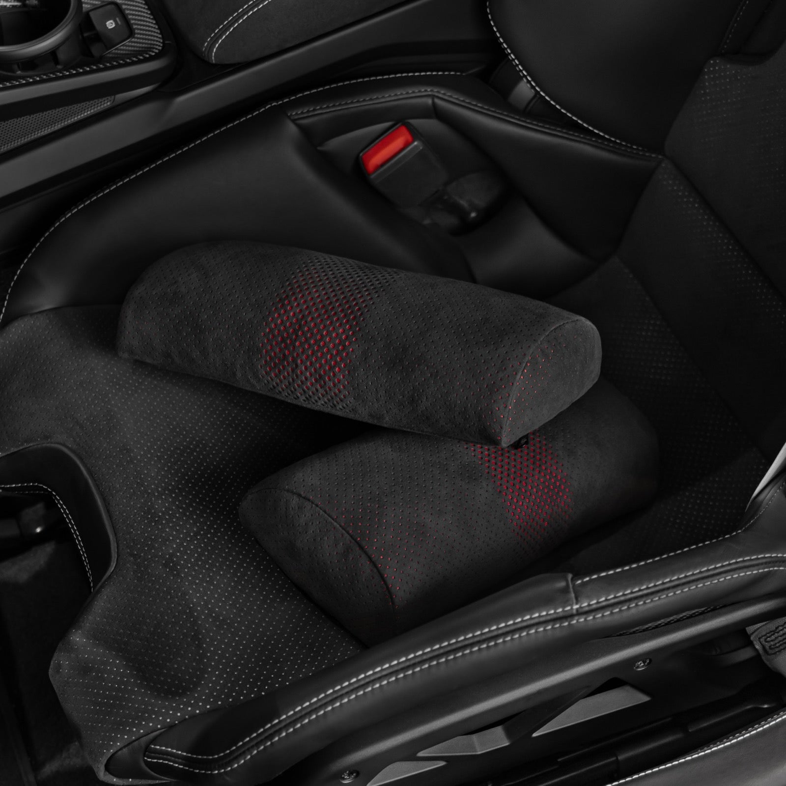 Two black Alcantara lumbar support pillows with red perforated dot pattern stacked in a Porsche 992.2 carbon bucket seat