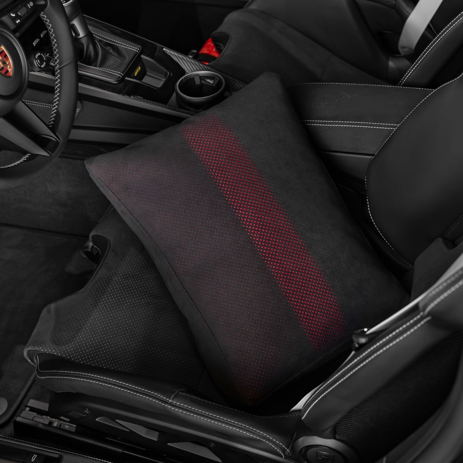 Black Alcantara space increase pillow with red dot perforation seated in the base of a Porsche 992.2 folding carbon bucket seat