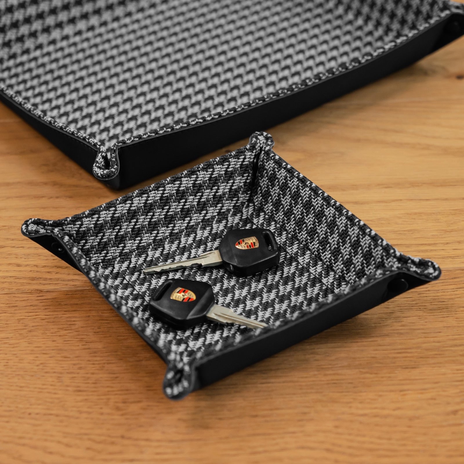 Black and white houndstooth leather valet tray holding two Porsche keys next to a larger tray
