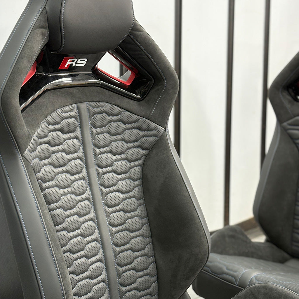 Audi RS bucket seat pair installed – gray Alcantara honeycomb panels with red RS headrest badge, driver and passenger