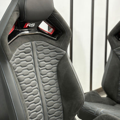 Audi RS bucket seat pair installed – gray Alcantara honeycomb panels with red RS headrest badge, driver and passenger