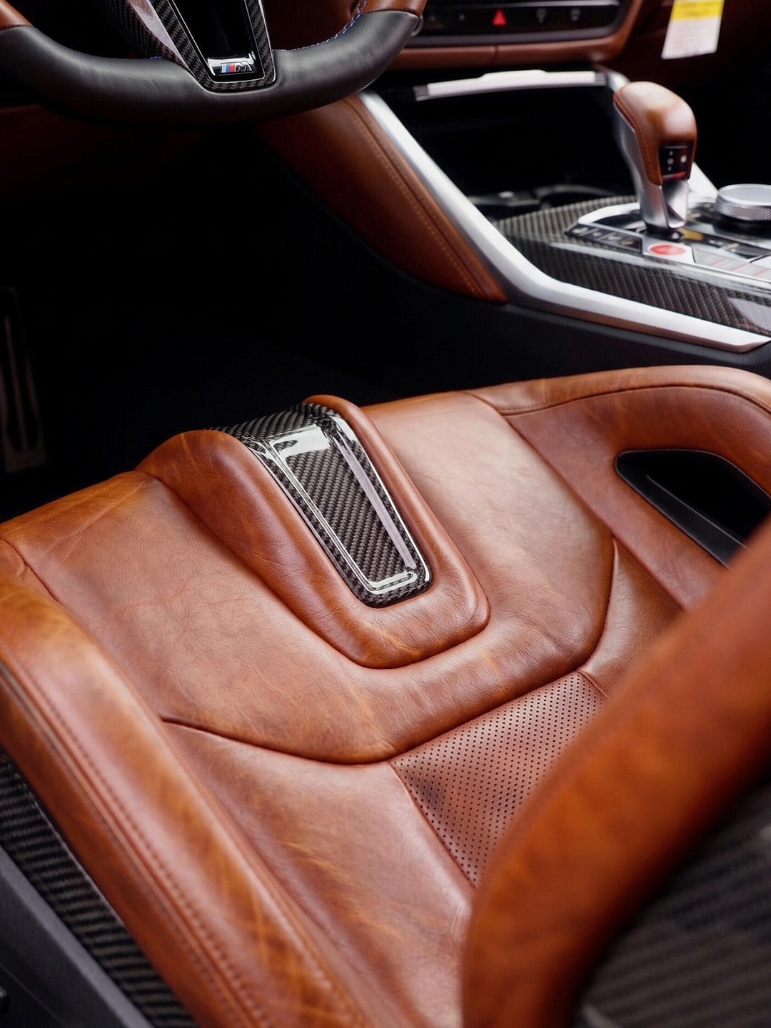 BMW M Carbon Fiber Bucket Seat in cognac wax pull-up leather, perforated cushion with carbon fiber trim and illuminated emblem, fitted in a BMW M interior