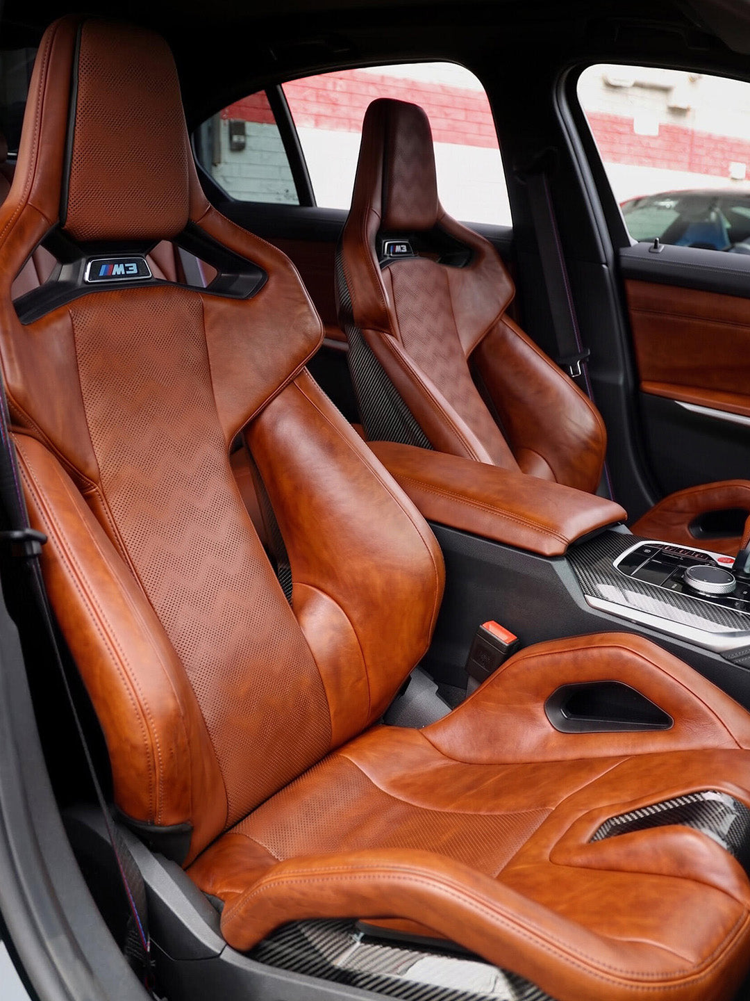Pair of BMW M3 G80 Carbon Fiber Bucket Seats in cognac wax pull-up leather with illuminated M3 headrest emblems and carbon shells, fitted in the car