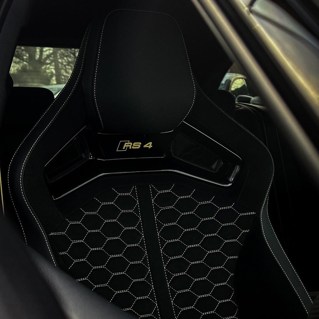 Audi RS4 aftermarket bucket seat installed – black Alcantara honeycomb quilting with gold RS4 headrest badge and white contrast stitching