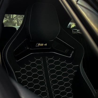 Audi RS4 aftermarket bucket seat installed – black Alcantara honeycomb quilting with gold RS4 headrest badge and white contrast stitching