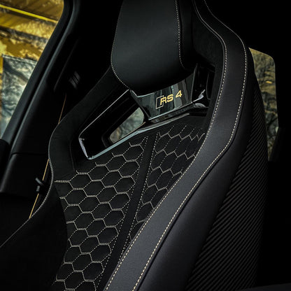 Audi RS4 bucket seat backrest close-up – hexagonal honeycomb quilted black Alcantara with gold RS4 badge, carbon fiber door panel visible