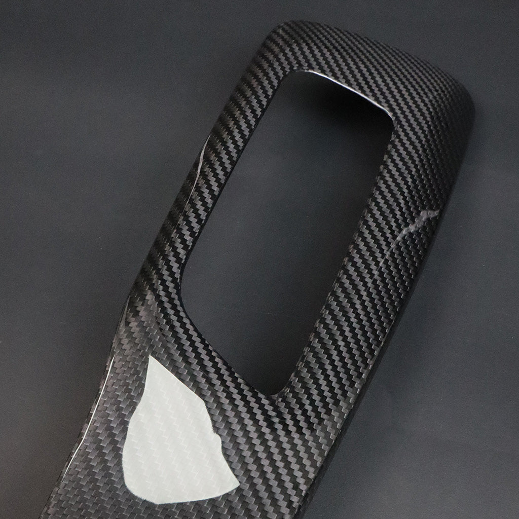 BMW G8X M2 M3 M4 Dry Carbon Side Seat Cover macro – single cover diagonal, protective film partially peeled showing 2x2 twill weave and gloss dry carbon finish