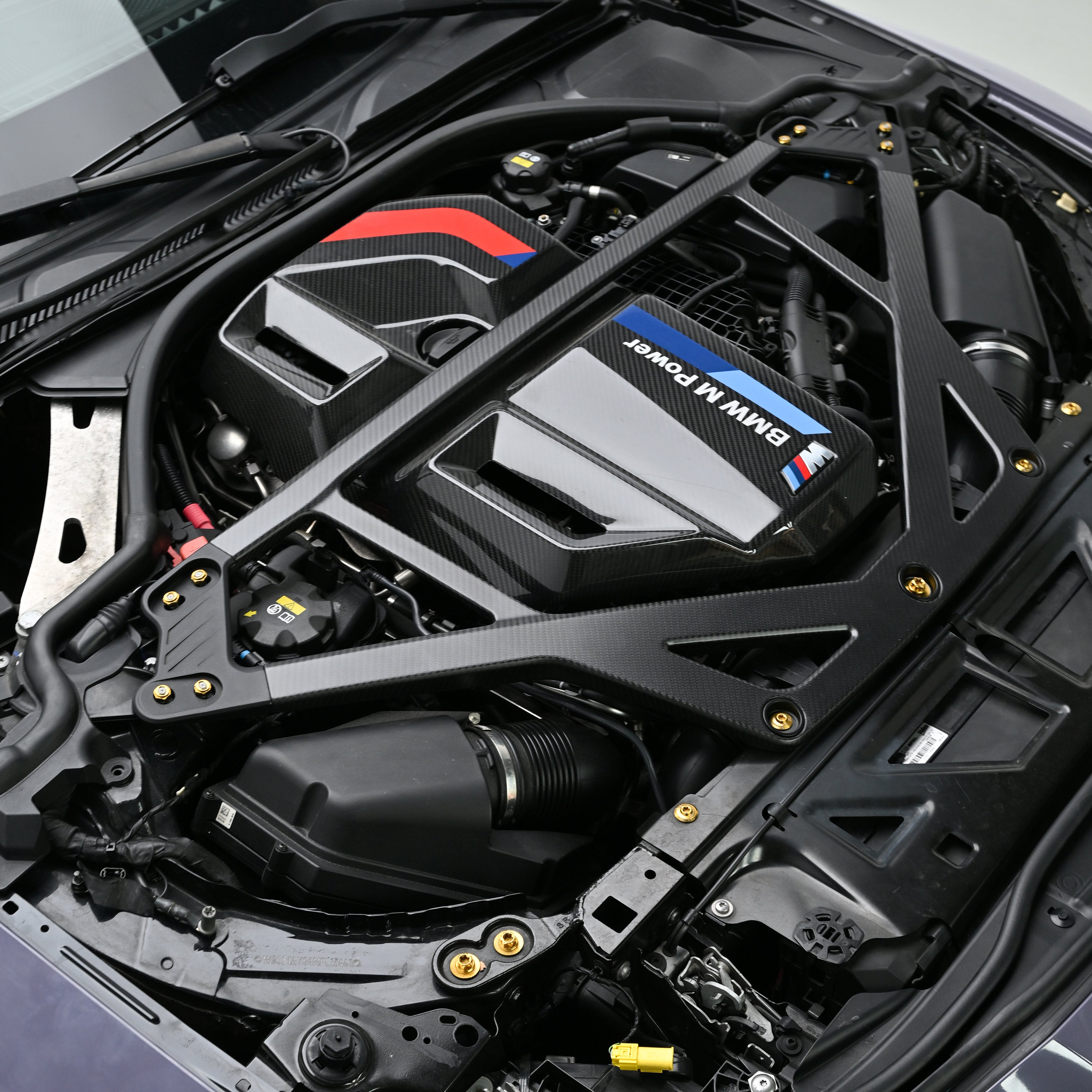 BMW G8X engine bay with black CSL style carbon fiber strut brace and Gold titanium bolts