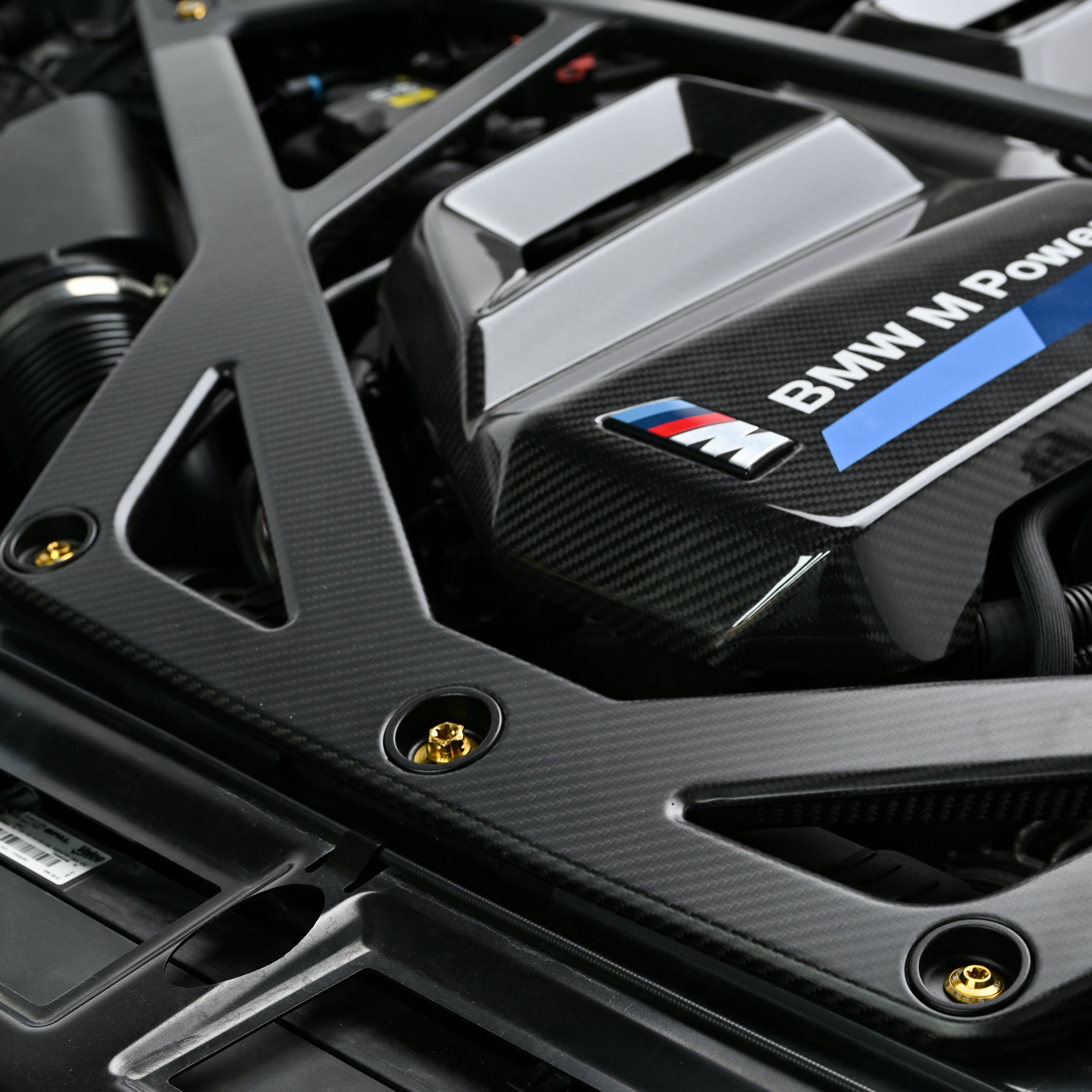 Black CSL style carbon fiber strut brace and Gold titanium bolts installed in a BMW G8X engine bay