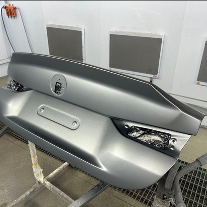 BMW G87 M2 CS carbon fiber trunk lid finished in solid silver grey OEM paint, full rear view on a paint booth stand