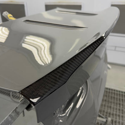 BMW G87 M2 CS carbon fiber trunk lid in grey OEM paint with the ducktail spoiler lip left in exposed clear coated carbon weave, a carbon stripe finish