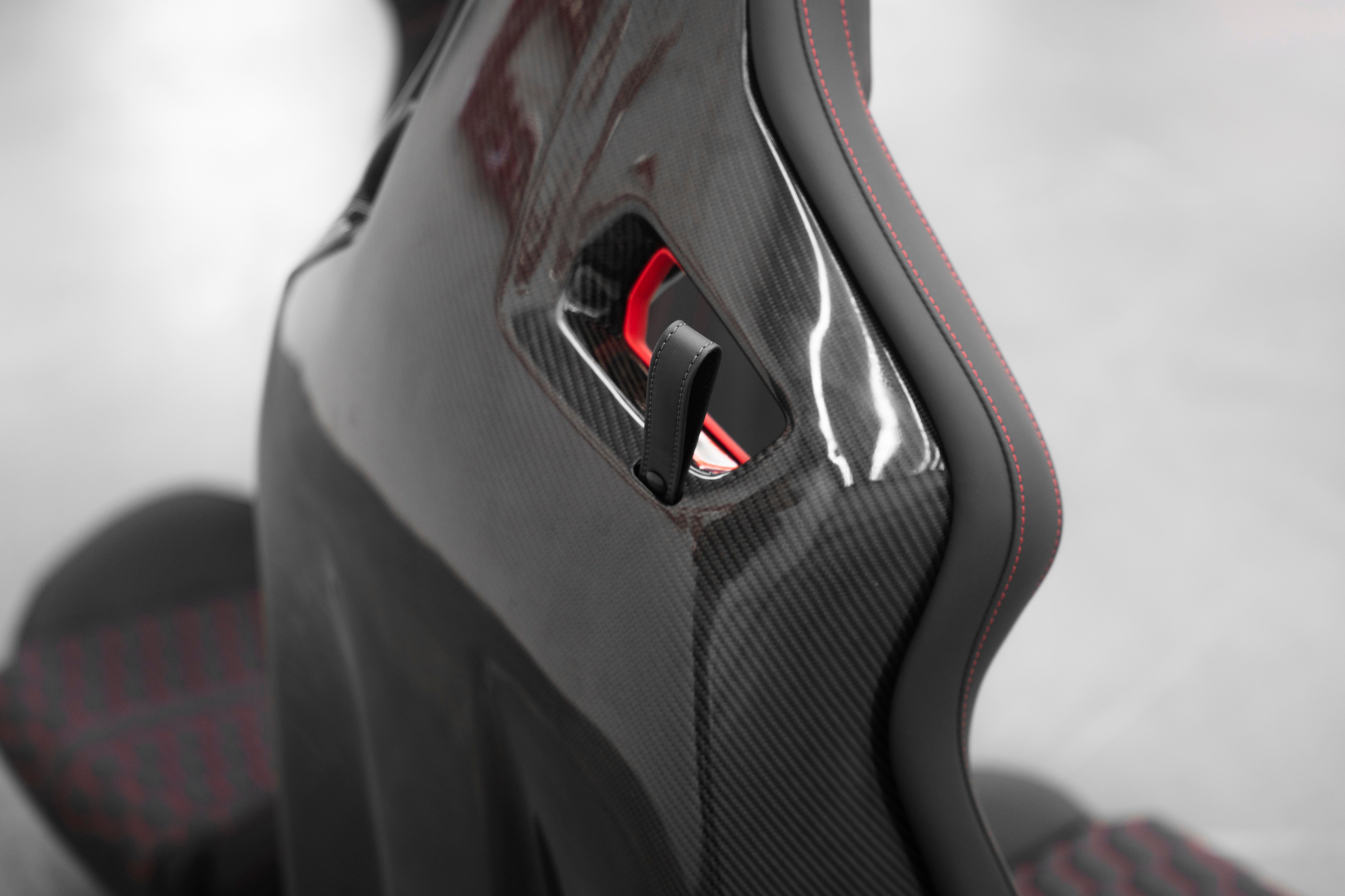 Audi R8 folding bucket seat carbon fiber backrest close-up with leather fold-release strap and red interior detail