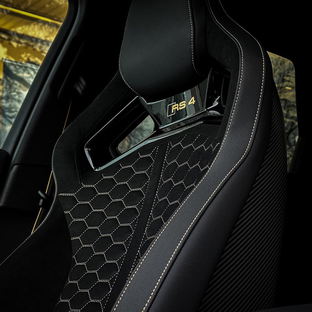 Audi RS4 bucket seat backrest close-up – black Alcantara honeycomb quilting, gold RS4 badge, carbon fiber door panel visible