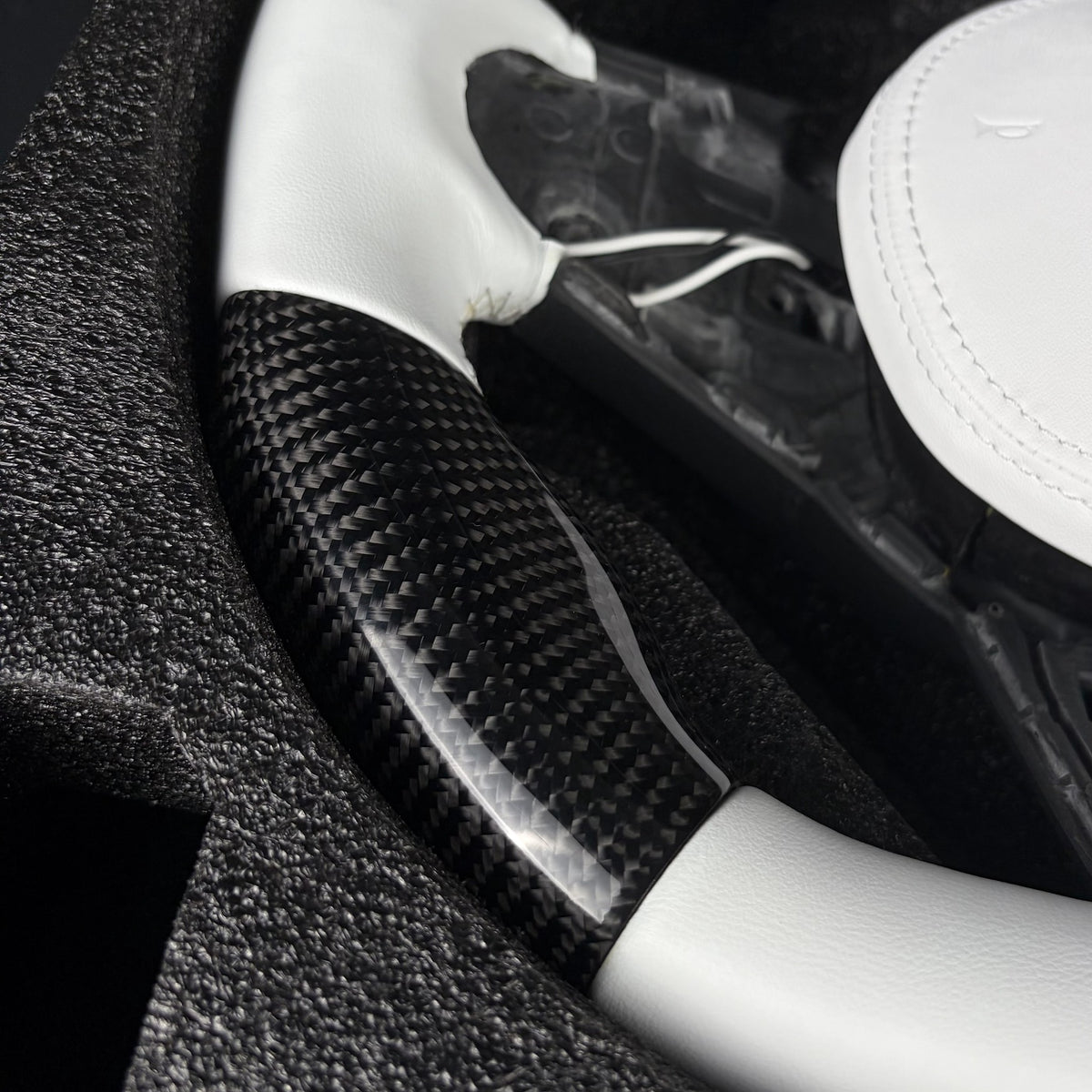 Twill carbon fiber lower rim section between the white leather grip and the flat bottom on the custom steering wheel