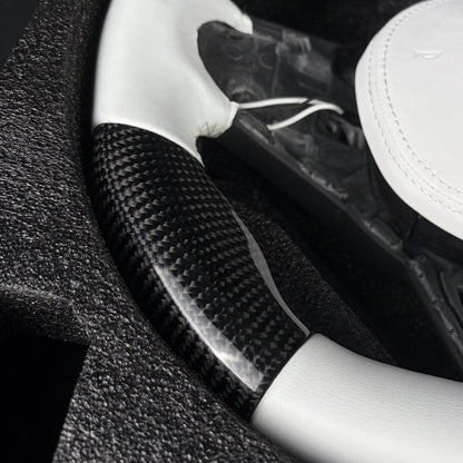 Twill carbon fiber lower rim section between the white leather grip and the flat bottom on the custom steering wheel