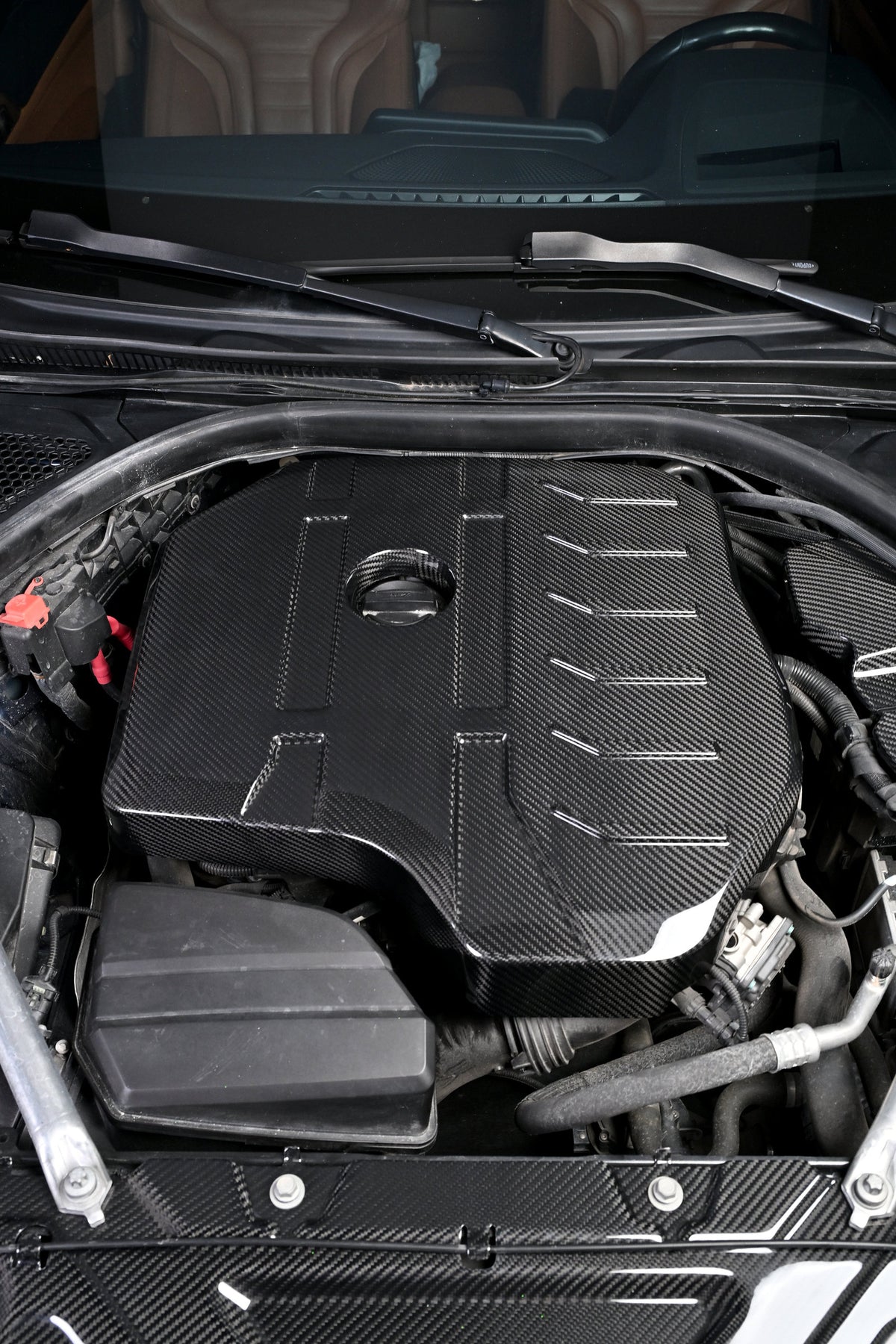 BMW G22 4 Series B48 carbon fiber engine cover is viewed from the front with the windshield visible above it.