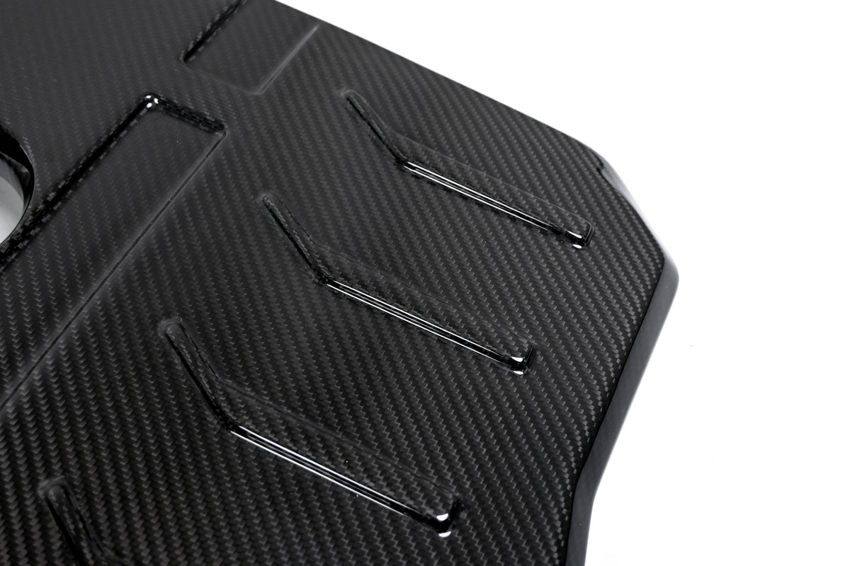 BMW G22 4 Series B48 carbon fiber engine cover is shown close up with raised ribs and the curved outer edge.