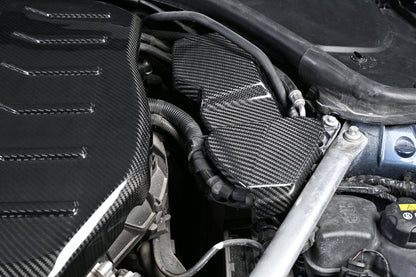 BMW G22 4 Series carbon fiber ECU battery terminal cover is shown installed beside the engine cover and hoses.