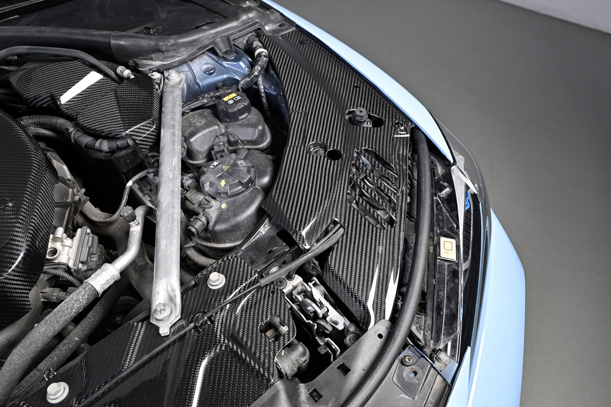 BMW G22 4 Series carbon fiber headlight cover panels are shown installed beside the blue bodywork and fluid tanks.