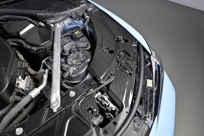 BMW G22 4 Series carbon fiber headlight cover panels are shown installed beside the blue bodywork and fluid tanks.