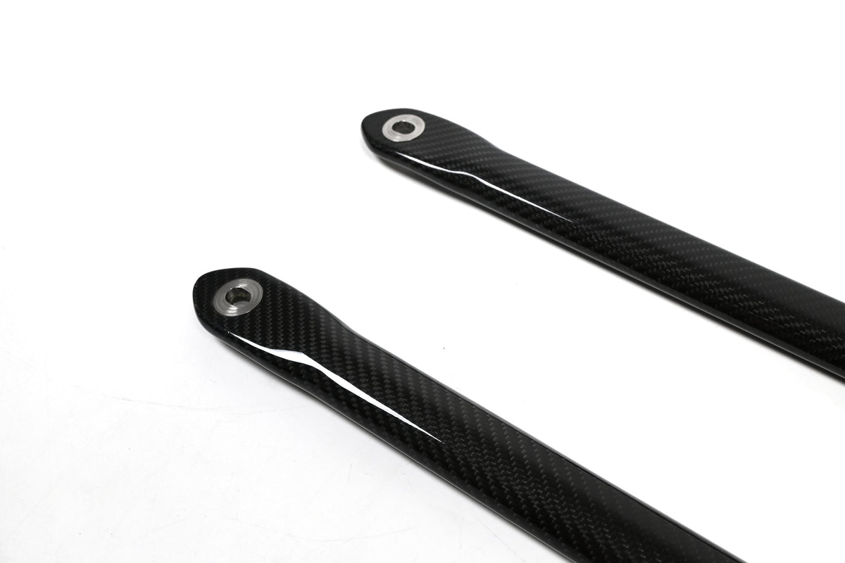 BMW G22 4 Series carbon fiber strut brace bars are seen close up with the left ends and round metal sleeves.