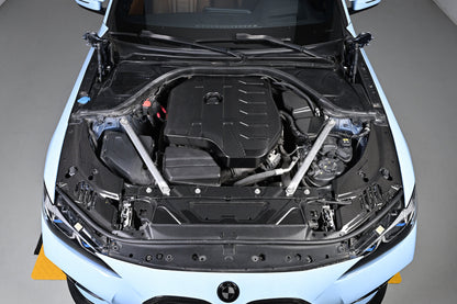 BMW 4 Series engine bay carbon fiber covers are seen from above the front of a blue car with the hood open.