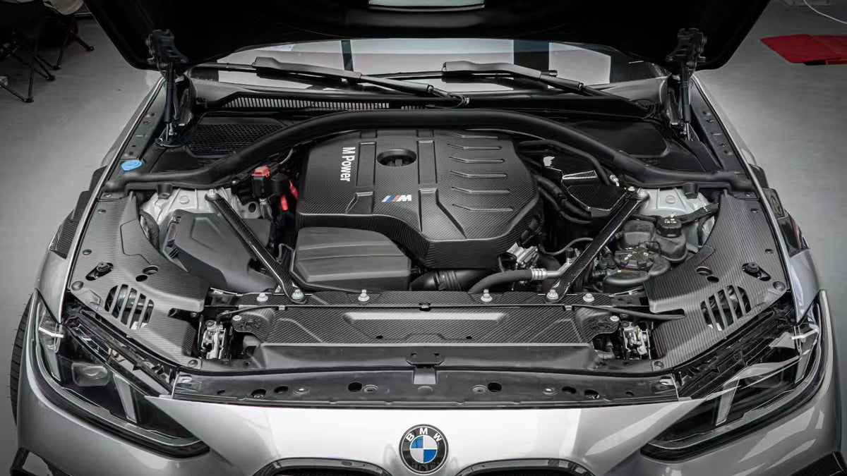 BMW 4 Series engine bay carbon fiber covers are shown from the front above the headlights of a silver car.