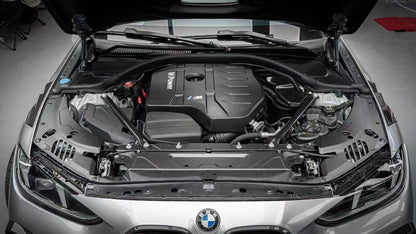 BMW 4 Series engine bay carbon fiber covers are shown from the front above the headlights of a silver car.