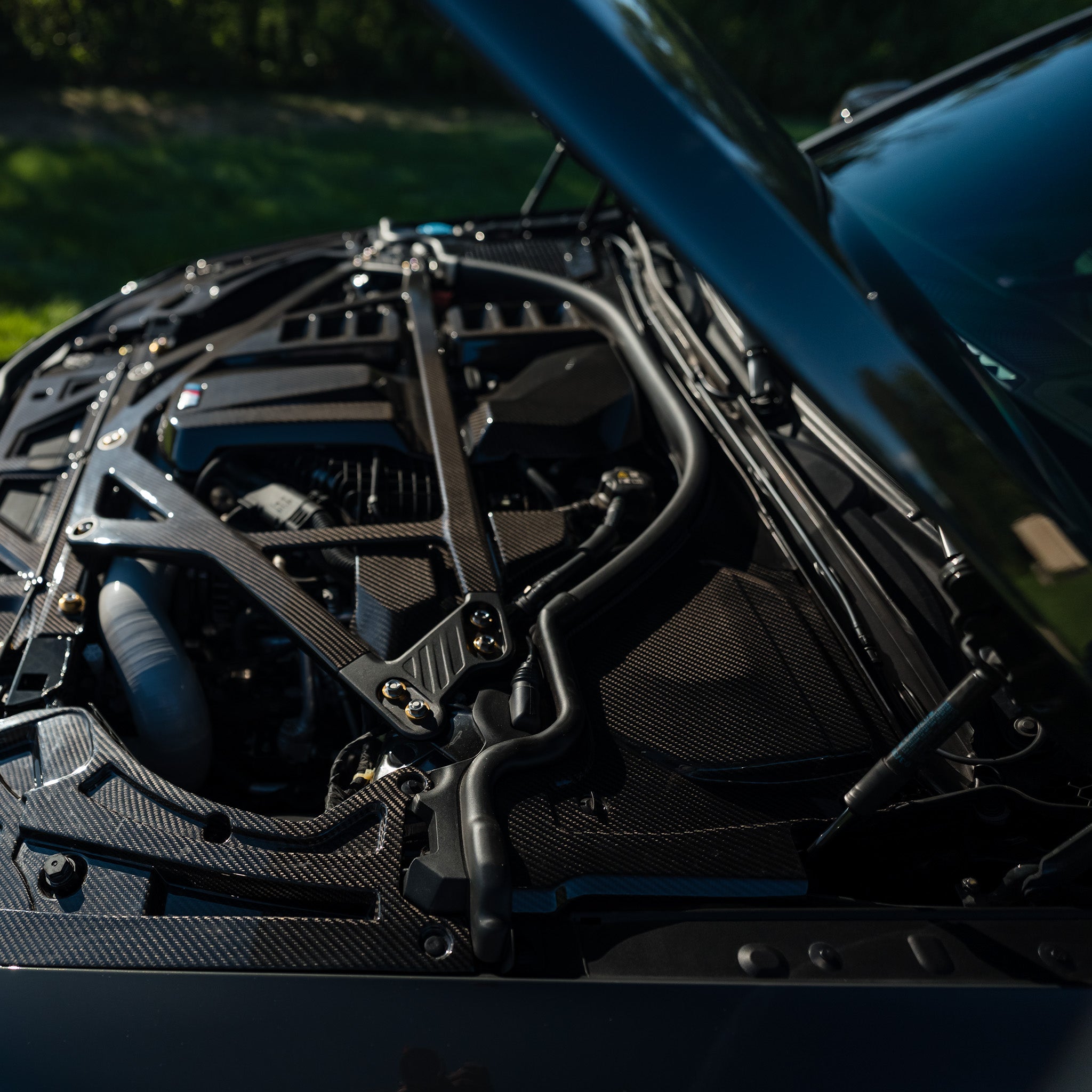 Side view of the carbon fiber cowl panel and black CSL style strut brace installed on a BMW G80 M3