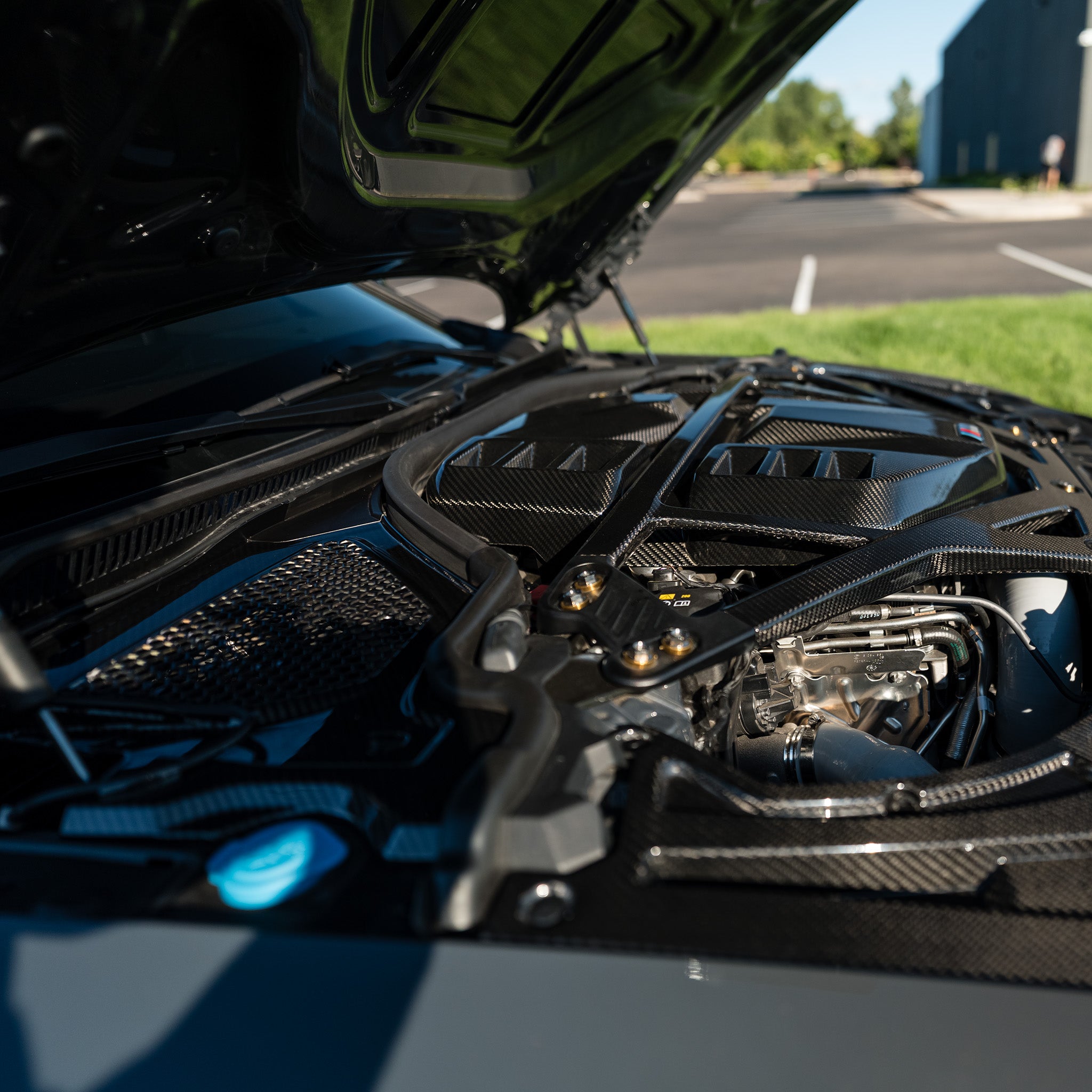Side detail of the OEM style carbon fiber engine cover and black CSL style strut brace on a BMW G80 M3