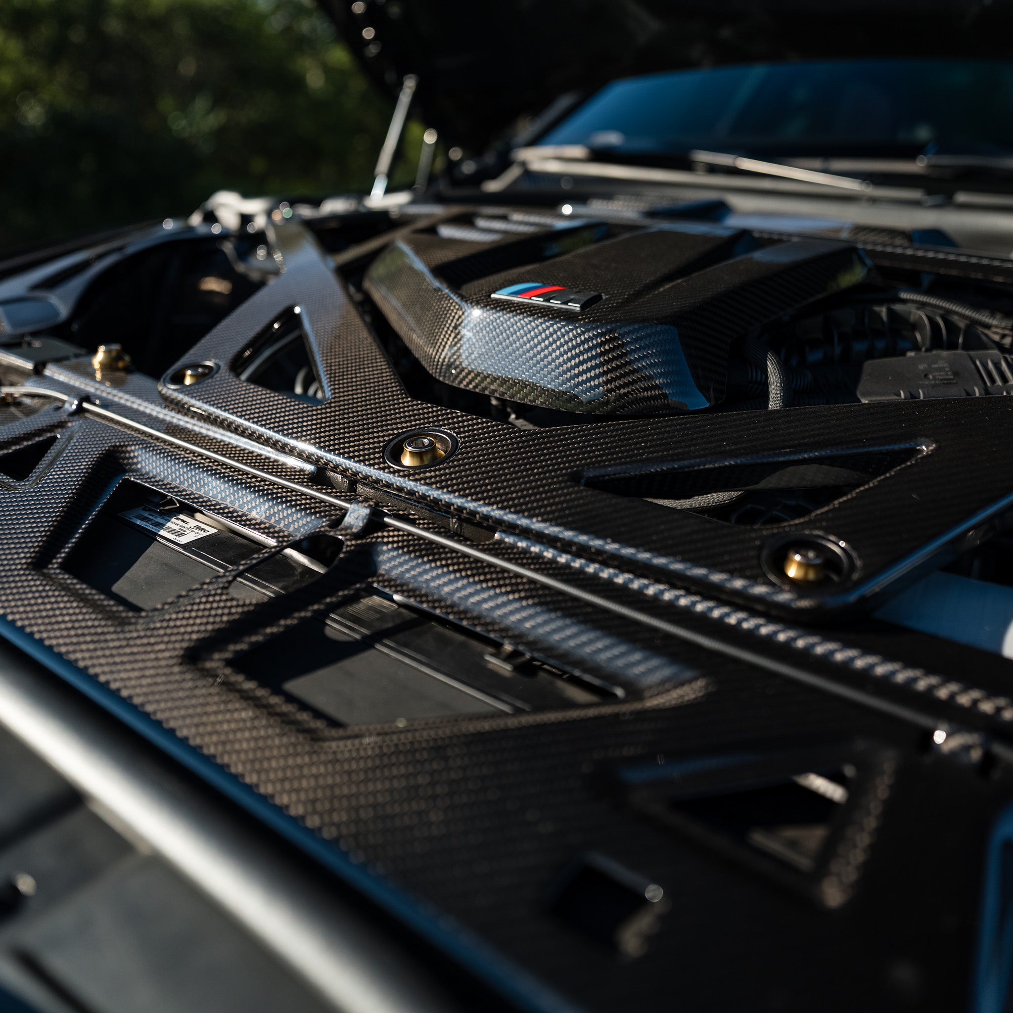 Close-up of the CSL style carbon fiber strut brace, cooling shroud, and Gold V2 titanium bolts on a BMW G80 M3