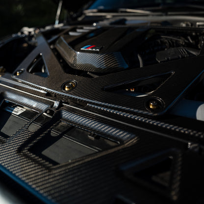 Close-up of the CSL style carbon fiber engine strut brace and Gold V2 titanium bolts on a BMW G80 M3