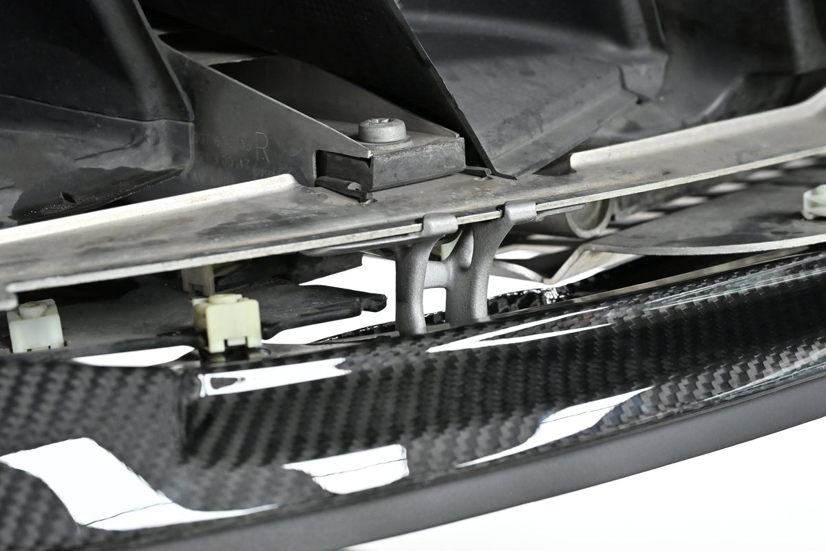 Underside view of the CSL style front lip held by its metal mounting bracket on a BMW G82 M4