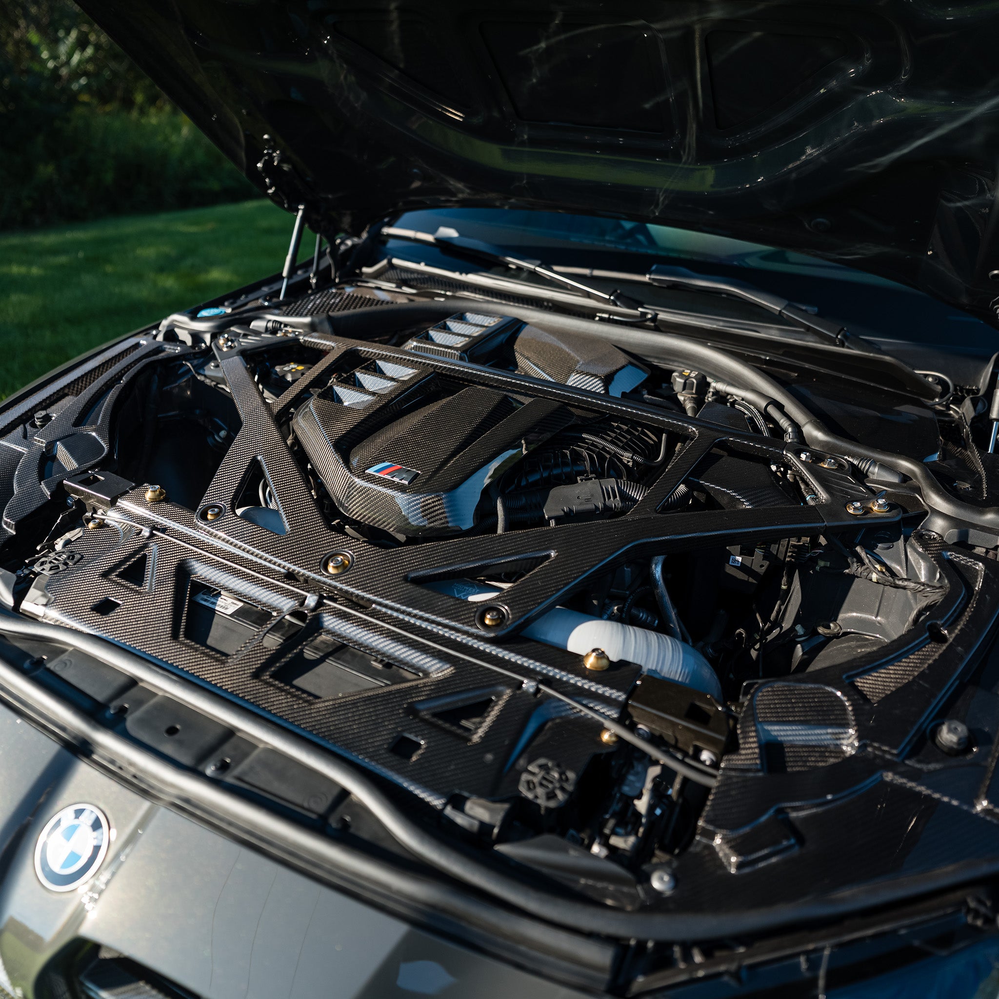 Three-quarter view of the RAG Spec carbon fiber engine bay kit installed on a BMW G80 M3