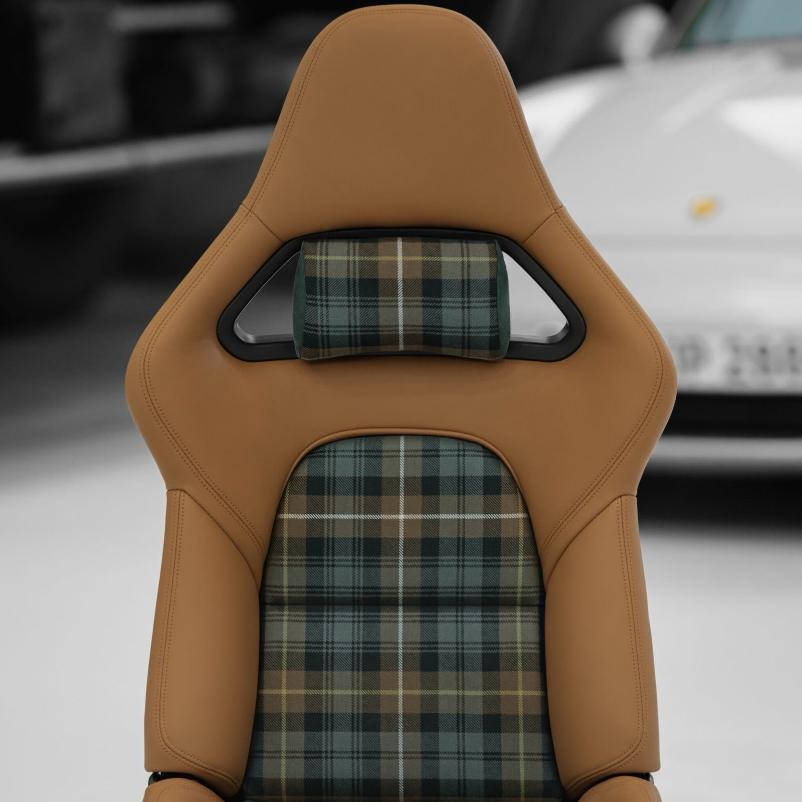 Green tartan headrest pillow mounted in the headrest opening of a tan leather Porsche 992.2 folding carbon bucket seat