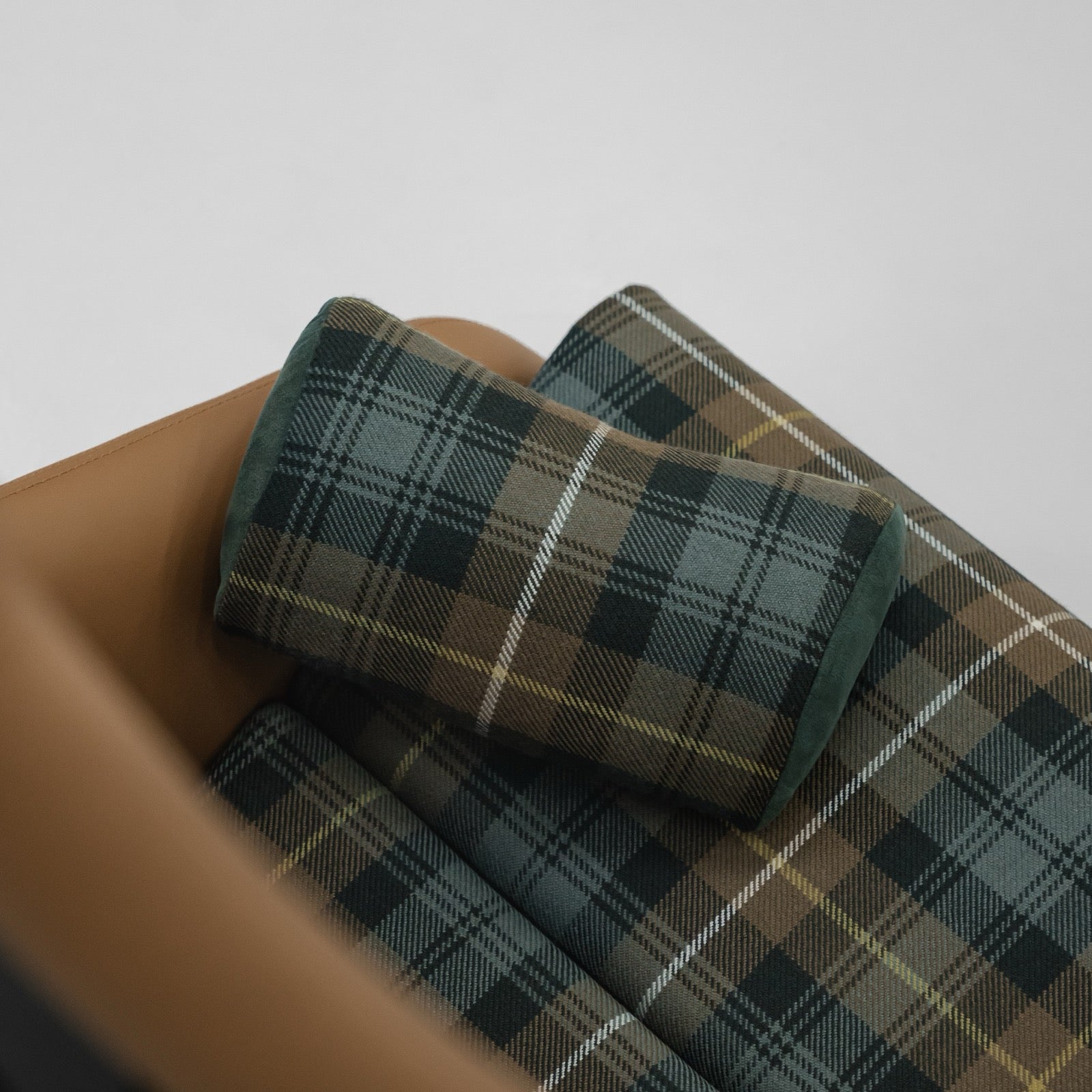 Two green and brown tartan Porsche headrest pillows resting on a tan leather folding carbon bucket seat