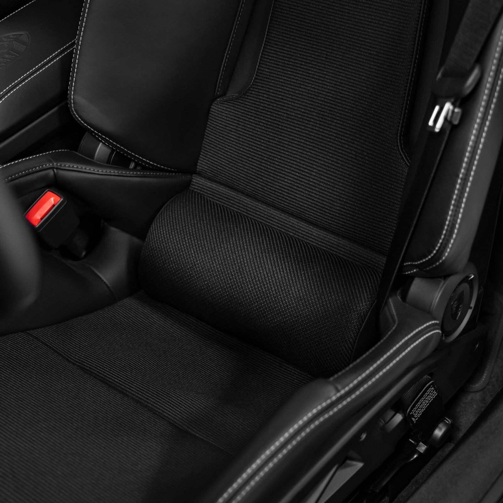 Close up of a black Alcantara lumbar support pillow with red perforated stitching installed in a Porsche 992.2 GT3 Touring carbon bucket seat
