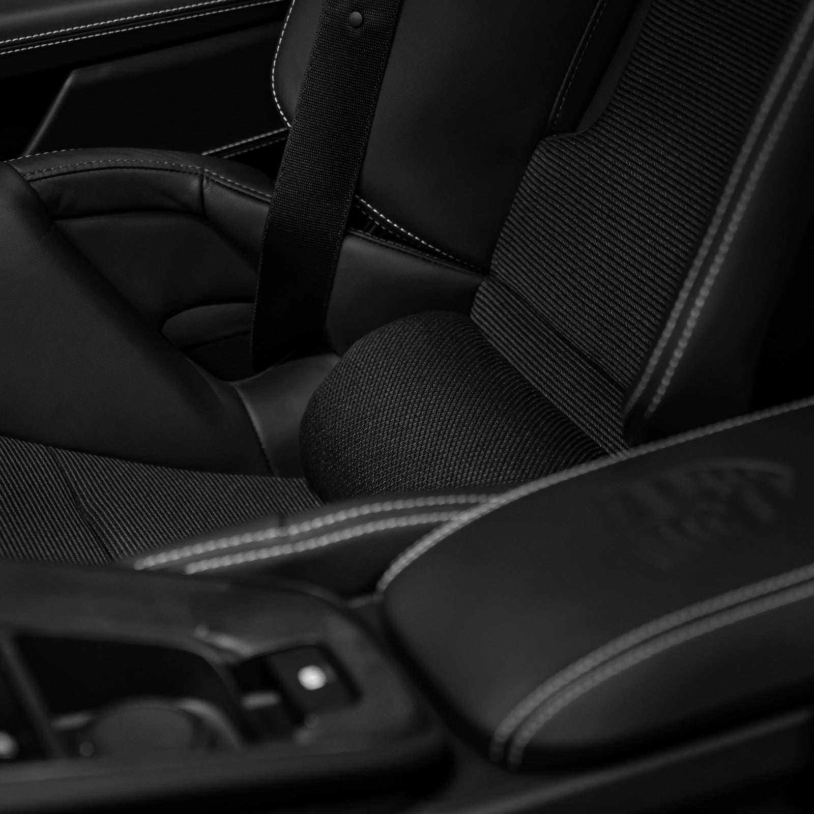 Black Alcantara lumbar support pillow with red dot perforation resting in the lower back of a Porsche 992.2 folding carbon bucket seat near the seatbelt buckle